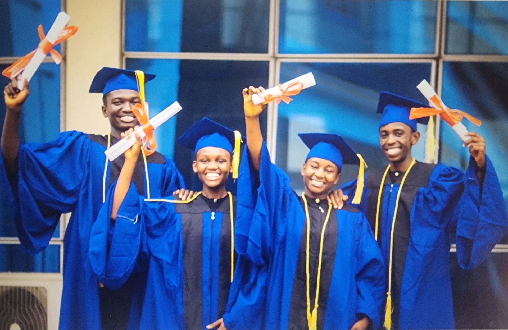 Four Charisma Tumaini students in blue caps and gowns raising their high-school diplomas after placing first among all countries at the Rochas Foundation